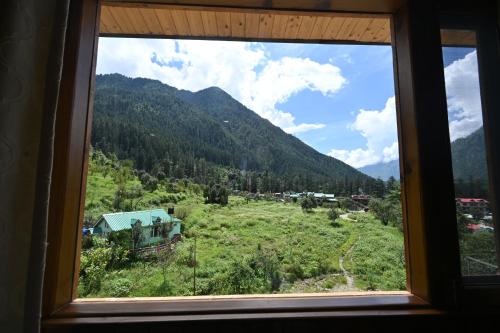 a window with a view of a field and a mountain at The Hillside in Kasol