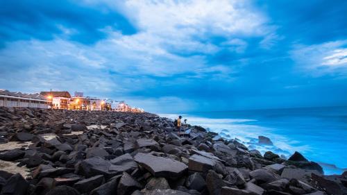 a man standing on a rocky beach near the ocean at Jeyam Residency in Puducherry