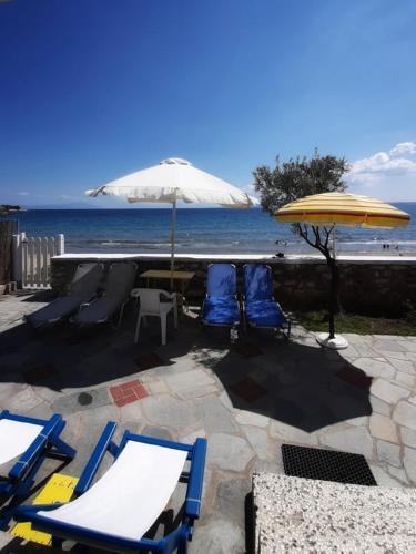 a patio with chairs and an umbrella and the beach at House Kokkalas on the beach in Pyrgadikia