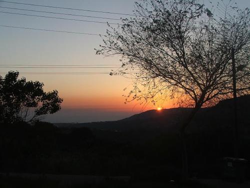 a sunset over a mountain with a tree in the foreground at Keshet Eilon - Suites and Villas in Elon