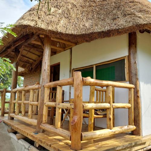 dom z dachem krytym strzechą i drewnianą werandą w obiekcie Songbird Safari Lodge & Campsite w mieście Katunguru