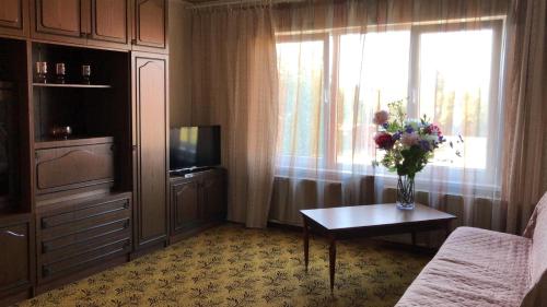 una sala de estar con TV y un jarrón de flores sobre una mesa en KULDIGAS 38 APARTMENTS, en Liepāja