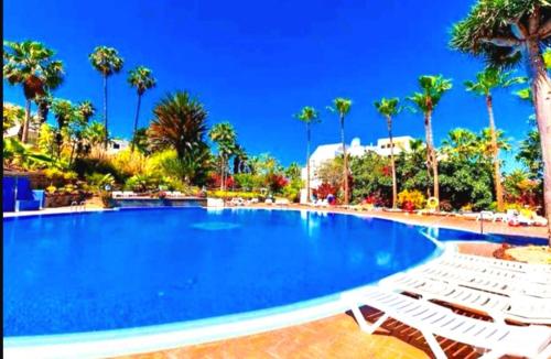 una grande piscina con sedie bianche e palme di ELDORADO 2 BEDROOMS a Playa de las Americas