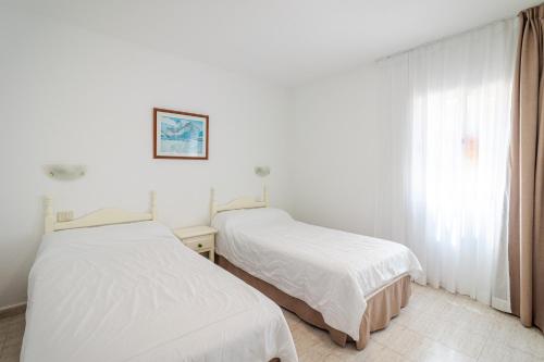 two beds in a white room with a window at Flatguest Alisios Playa 4 in Corralejo