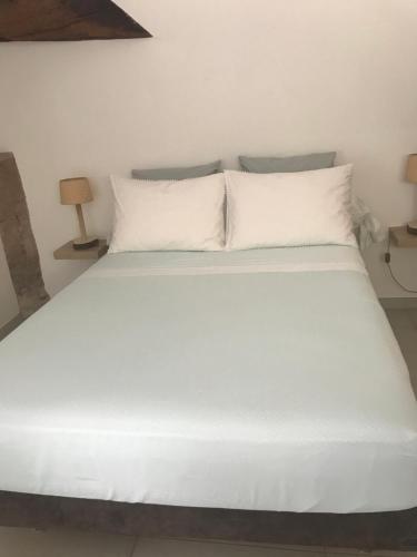 uma cama com lençóis brancos e almofadas num quarto em Ma maisonnette em Allauch