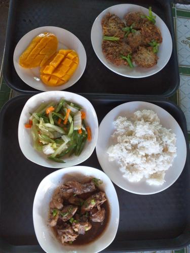 quatro pratos de comida num tabuleiro com arroz e legumes em Junior & Nemesia's Cottages em Baclayon