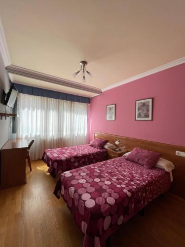 2 Betten in einem Zimmer mit rosa Wänden in der Unterkunft Hostal Santiago 2 in Burgos