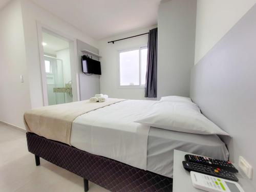 a white bedroom with a large bed and a desk at Hospeda Mariscal Flat in Bombinhas
