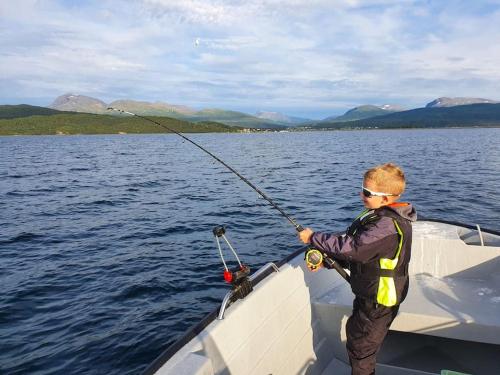 a boy standing on a boat holding a fishing rod at Off-the-grid cabin on the island of Senja in northern Norway in Vangsvik