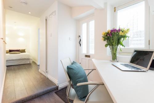 Cette chambre blanche comprend un bureau avec un ordinateur portable et des fleurs. dans l'établissement Paddington/Lancaster Gate Luxury Apartment by Hyde Park, à Londres