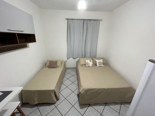 two beds in a small room with a window at KITNET ACONCHEGANTE A 3 MINUTOS DA PRAIA in Guarapari