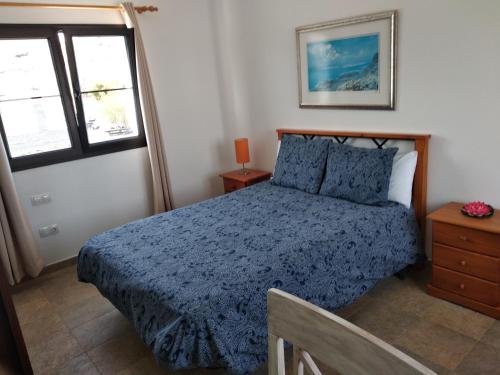a bedroom with a bed with a blue comforter and two windows at Finca la Tabaiba piscina compartida adultos in Máguez