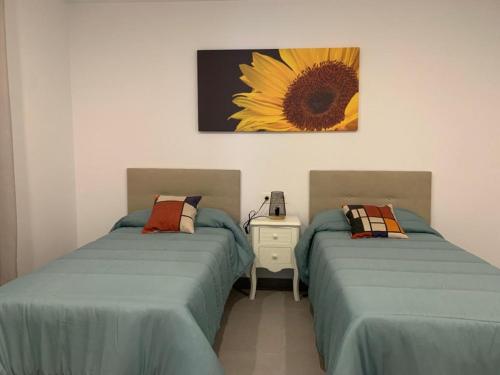 dwa łóżka w pokoju z obrazem słonecznika na ścianie w obiekcie APARTAMENTO ENCANTO II w mieście Conil de la Frontera