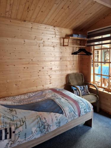 a bedroom with a wooden wall with a bed and two chairs at Slaaphuisjes LauwersmeerPlezier! in Lauwersoog