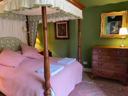 a bedroom with a canopy bed with a dresser and a mirror at Neidpath Castle Cottage in Peebles