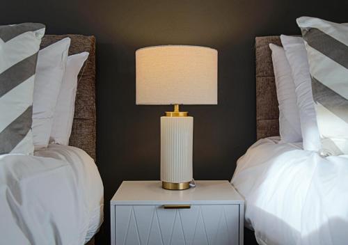 a lamp on a night stand next to two beds at Stylish House with Smart TVs and Netflix, Fast Wifi, Free Parking and Garden by Yoko Property in Milton Keynes