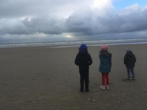 three people standing on the beach looking at the ocean at Chouette appartement 5 personnes in De Haan