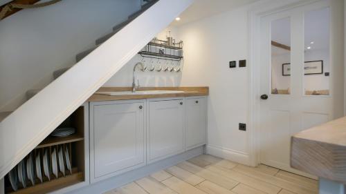 a kitchen with white cabinets and a staircase at Padstow Escapes - Captains Cottage in Padstow