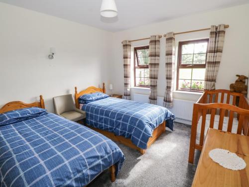 a bedroom with two beds and a table and two windows at Belladrihid Cottage in Ballysadare