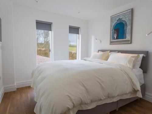 a white bedroom with a large bed and a window at The Bothy in Slapton