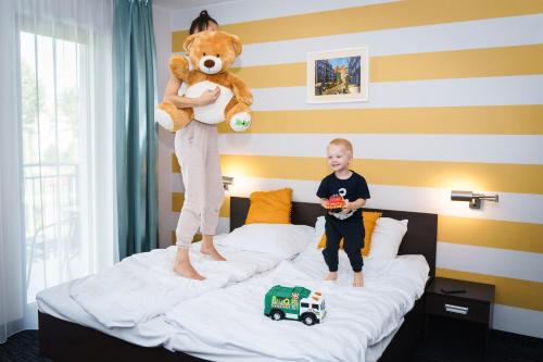 Um rapaz está de pé numa cama com um urso de peluche. em Golden Tulip Gdańsk Residence em Gdansk
