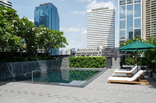 a swimming pool with two lounge chairs and an umbrella at Maitria Hotel Sukhumvit 18 Bangkok – A Chatrium Collection in Bangkok