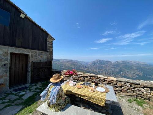 a woman sitting at a table on top of a mountain at Tiñones cabaña pasiega in Valcaba