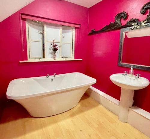 Baño de color rosa con bañera y lavamanos en The Timber Barn South Downs West Sussex Sleeps 18 en Hardham