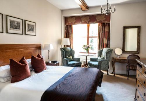 a bedroom with a bed and two chairs and a window at Ettington Park Hotel, Stratford-upon-Avon in Stratford-upon-Avon