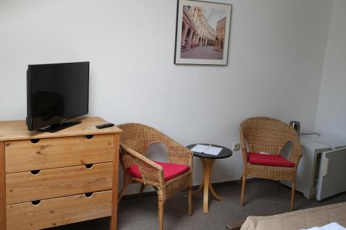 um quarto com duas cadeiras e uma cómoda com uma televisão em Penzión Malý Dvor em Štúrovo