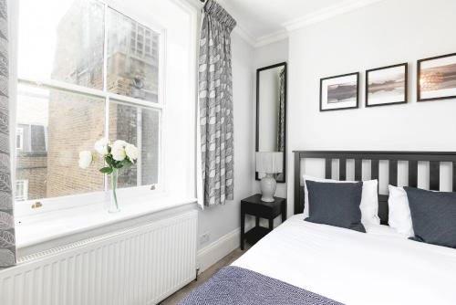 a bedroom with two beds and a window with a vase of flowers at PenthouseStays Notting Hill - Chic 2 Bedroom Apartment w/ King Beds - near Portobello Road & Kensington High Street in London