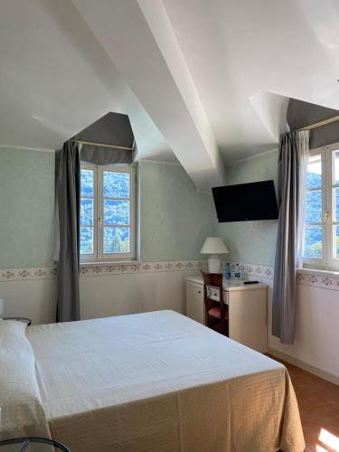 a bedroom with a white bed and two windows at Caroline Hotel in Brusimpiano