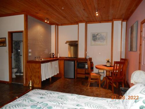 1 dormitorio con 1 cama y cocina con mesa en Self-contained Cabin 10 min to Huskisson en Tomerong