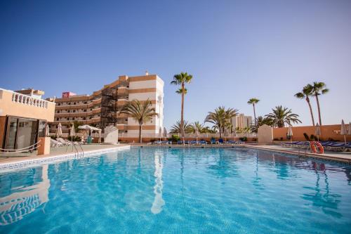 a large swimming pool with palm trees and buildings at Servatur Caribe in Playa de las Americas
