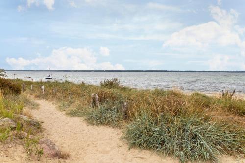 a dirt path leading to a beach with a boat in the water at Gartenglückchen in Lindhöft