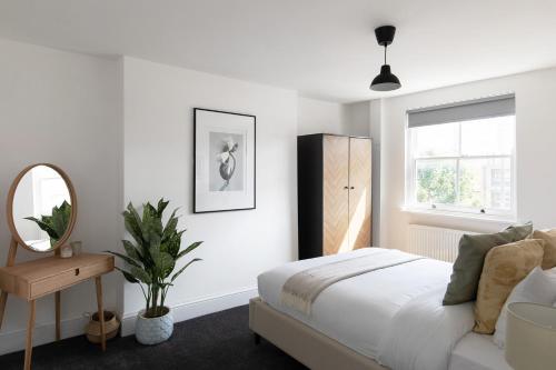 a white bedroom with a bed and a mirror at The Camberwell Retreat - Alluring 2BDR Flat with Garden in London