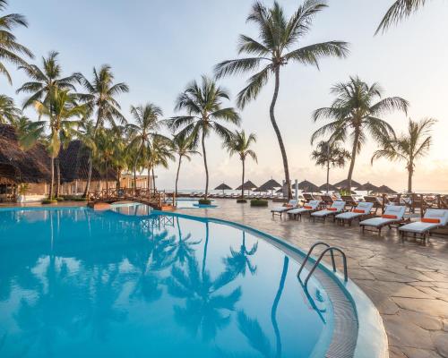 a swimming pool with chairs and palm trees at Kiwengwa Beach Resort in Kiwengwa