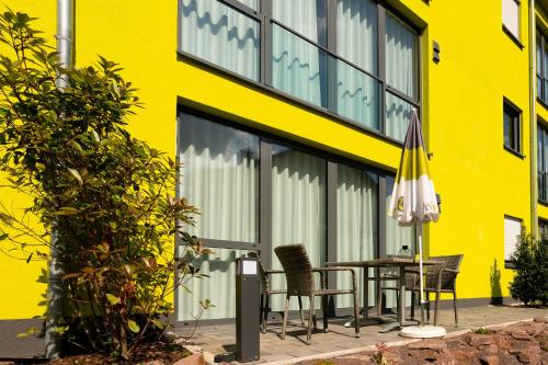 a yellow building with a table and chairs and an umbrella at Vis Saar Vie - Ferienwohnungen an der Saarschleife in Mettlach