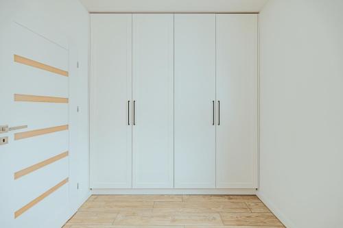 a white kitchen with white cabinets and a wooden floor at Apartament Szlachecka in Warsaw