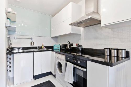 a kitchen with white cabinets and a washer and dryer at Modern 2 Bedroom Apartment in Hoxton in London