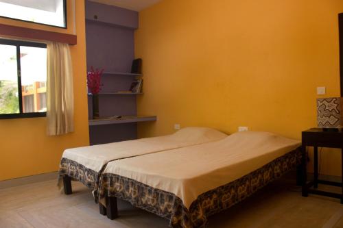 a bedroom with a bed with yellow walls and a window at Auromode Apartments Auroville in Auroville