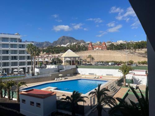 a large swimming pool with palm trees and a building at Precioso apartamento en 5 minutos de la playa in Playa de las Americas