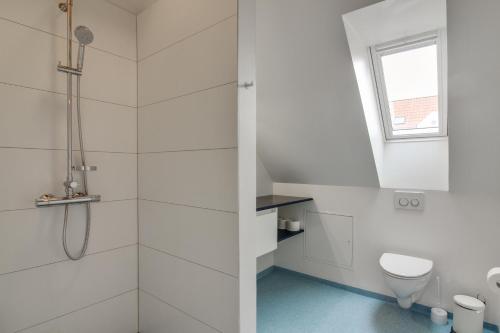 a white bathroom with a toilet and a window at Skudehandelen. in Lønstrup