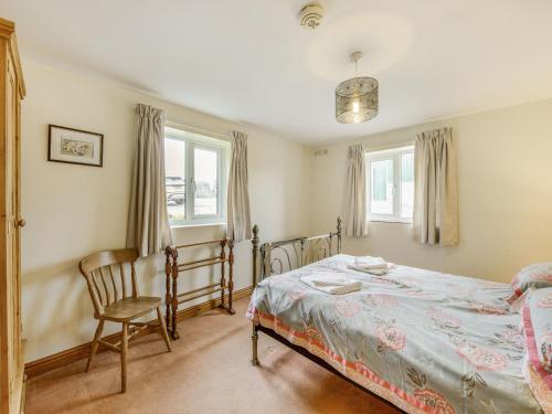 a bedroom with a bed and a chair and windows at Lark's Rise Cottage in Onecote