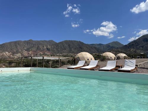 a swimming pool with chairs and mountains in the background at Denmoza Eco Lodge in Potrerillos