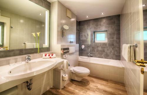 a bathroom with a sink and a toilet and a tub at Leonardo Hotel Hamburg Airport in Hamburg