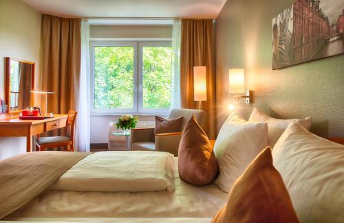 a hotel room with a bed and a desk and a window at Leonardo Hotel Hamburg Airport in Hamburg