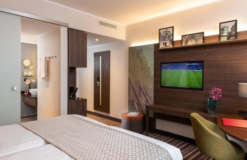 a hotel room with a bed and a television on a wall at Leonardo Hotel Bad Kreuznach in Bad Kreuznach