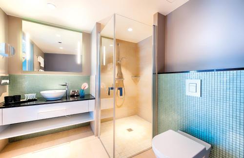 ein Bad mit einer Dusche, einem WC und einem Waschbecken in der Unterkunft NYX Hotel Munich by Leonardo Hotels in München