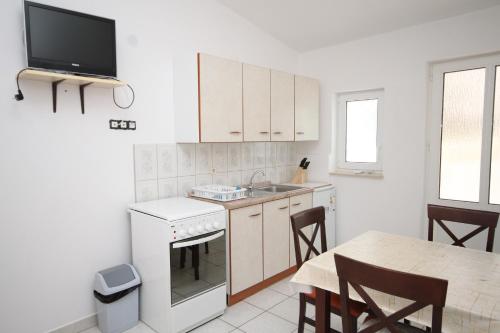 een keuken met witte kasten en een tafel en een tv bij Apartments by the sea Metajna, Pag - 6336 in Metajna